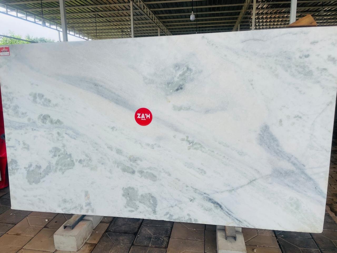 A full white marble slab with grey and green veining, standing in the yard
